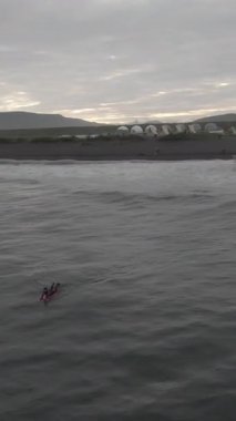 İnsansız hava aracından sörfçüler. Görüntü. Sörfçü selamlar ve dalgalar. Bir grup sörfçü. Gri manzara, hüzünlü hava. Hava aracı görüntüsü. Tanınmayan insanlar