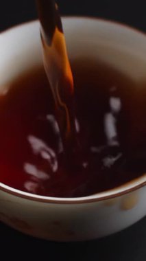 Yakın plan görüntüsü, koyu bir arkaplanda duran el değmemiş beyaz bir fincana sıcak çay döküldüğünü gösteriyor. Medya