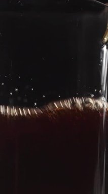 Kahveyle dolu cam bir sürahi, koyu bir zemine karşı zengin renkler ve kabarcıklar sergiliyor. Medya