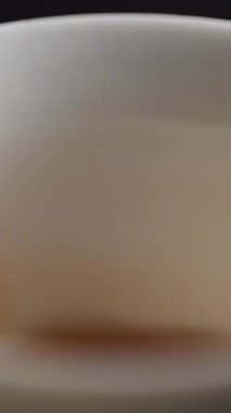 Dumanı tüten sıcak bir içeceğin yakın plan görüntüsü. Koyu bir arka plana ustalıkla beyaz bir bardağa dolduruluyor. Medya