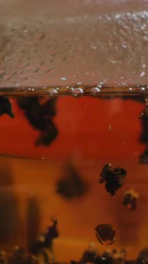 Ahşap bir masada, cam çaydanlık dolusu taze demlenmiş çaydanlıkla huzurlu bir ortam. Kapanışlar narin tasarımını sergiliyor ve rahatlatıcı bir atmosfer yaratıyor. Medya