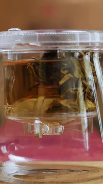 Huzurlu bir sahne, bir insan cam çaydanlığa buğulanmış çay dökerken, içeceğin sıcak tonlarını göstererek, bir sükunet anı yaratıyor. Medya