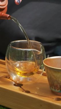 Geleneksel bir çaydanlıktan buharda pişirilmiş çayı el yapımı ahşap bir tepside narin bir fincana doldurarak sakin ve dikkatli bir atmosfer yaratıyor. Medya