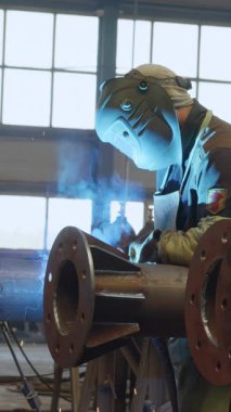 Güvenlik donanımı giyen yetenekli bir zanaatkar, endüstriyel bir ortamda metal bir boru üzerinde gerekli görevleri yerine getiriyor. Medya