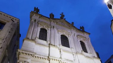 Heykelleri ve aydınlık pencereleri olan beyaz kilise cephesi alacakaranlık mavisi gökyüzüne karşı