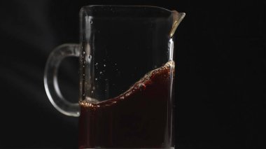Kahveyle dolu cam bir sürahi, koyu bir zemine karşı zengin renkler ve kabarcıklar sergiliyor. Medya