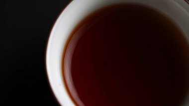 Zengin ve aromatik çayla dolu, koyu arkaplana karşı derin tonunu vurgulayan zevkli bir fincanın yakın çekimi. Medya