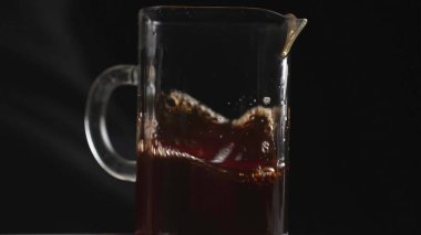 Kahveyle dolu cam bir sürahi, koyu bir zemine karşı zengin renkler ve kabarcıklar sergiliyor. Medya