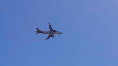 Beyaz ve kırmızı yolcu uçakları açık mavi gökyüzünde uçuyor ve dönüyor.