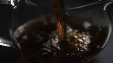 Koyu renkli bir sıvının zarif bir şekilde camdan bir çaydanlığa dökülmesi zengin renklerini gözler önüne seriyor. Medya
