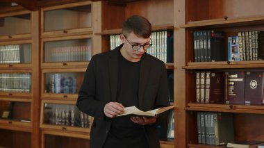 Düşünceli genç bir adam rahat ve davetkar bir kütüphanenin içinde raflarla çevrili bir kitap okumaya dalmış. Medya