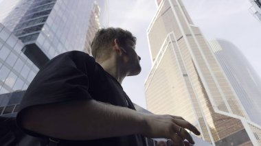 Modern gökdelenlerin yanında yürüyen iş adamı, akıllı telefon kullanıyor ve telefonla konuşuyor.