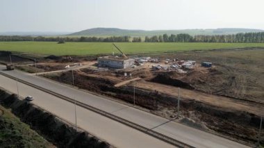 İnşaat işçileri otoyolun yakınına vinç kaldırma malzemeleri ile yeni bir yapı inşa ediyorlar.