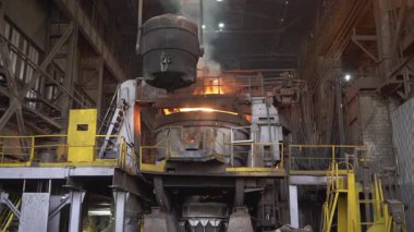 Asılı bir konteynırdan, çelik fabrikasındaki bir fırına sıvı metal dökülüyor.