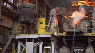 Erimiş metal, çelik fabrikasında büyük bir konteynırdan fırına dökülerek duman ve kıvılcımlar oluşturur.