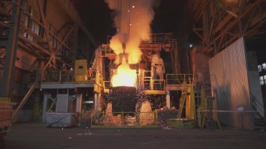 Çelik fabrikasındaki büyük bir konteynırdan dökülen erimiş metal kıvılcımlar ve duman yaratır.