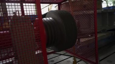 Büyük endüstriyel vinç bir fabrikada kırmızı koruma ızgarasının arkasında dönüyor.