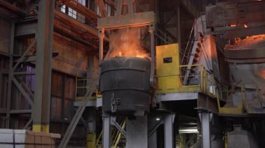 Erimiş çelik kepçe endüstriyel vinçle taşınıyor.