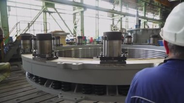 Fabrika işçisi büyük dairesel bir endüstriyel bölümü inceliyor ve notlar alıyor.