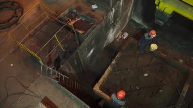 Endüstriyel işçiler fabrika ortamında büyük bir konteynıra dökülen karışımı denetliyor.