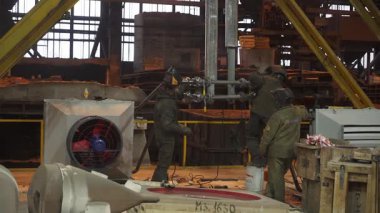 Endüstriyel işçiler, özel ekipman kullanarak, bir fabrikada metal bir yapıyı kaynak yapıyorlar.