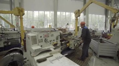Torna makinesi işleten yetenekli bir fabrika işçisi, işlek bir fabrikada metal parçaları üretiyor.