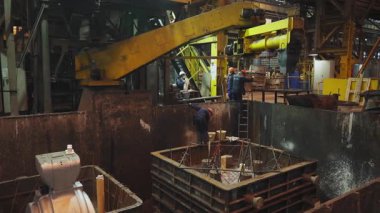 Metalürji işçileri ağır bir endüstriyel ortamda erimiş metal dökmek için bir kalıp hazırlıyorlar.