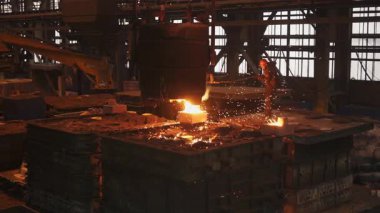 Erimiş metal, büyük bir konteynırdan bir kalıba dökülüp endüstriyel dökümhanede kıvılcım ve yoğun ısı yaratıyor.
