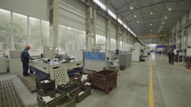 Fabrika işçisi makine işliyor ve büyük bir fabrikada yürüyor.