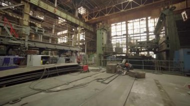 Yetenekli bir metal işçisi, yoğun bir fabrikanın içinde büyük bir metal bileşeni oluşturmak için özel ekipman kullanıyor.