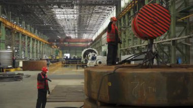 Mühendisler çelik fabrikasında büyük bir metal bileşeni üzerinde çalışırken el işaretleriyle iletişim kurarlar.