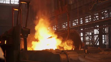 Çelik fabrikasındaki büyük bir konteynırdan dökülen erimiş metal kıvılcımlar ve duman yaratır.