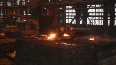 Dökümhane işçileri büyük bir endüstriyel kalıba erimiş metal döküyorlar.