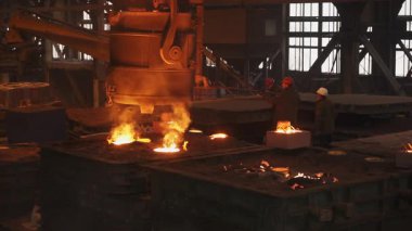 Dökümhane işçileri yoğun endüstriyel ortamda erimiş metali kalıplara dikkatlice döküyorlar.