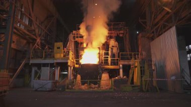 Çelik fabrikasındaki büyük bir konteynırdan dökülen erimiş metal kıvılcımlar ve duman yaratır.