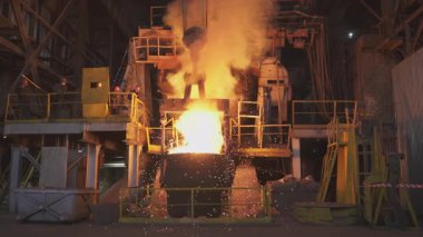 Çelik fabrikasındaki büyük bir konteynıra erimiş metal döküp kıvılcım ve duman çıkaran endüstriyel bir süreç.