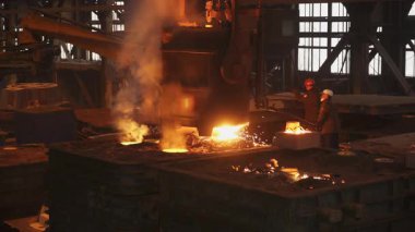 Dökümhaneye erimiş metal döken çelik işçileri kıvılcım ve duman yaratıyor.