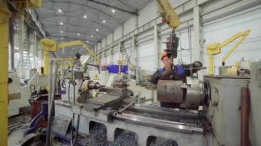 Torna makinesi işleten yetenekli bir metal işçisi modern bir endüstriyel fabrikada hassas parçalar üretiyor.