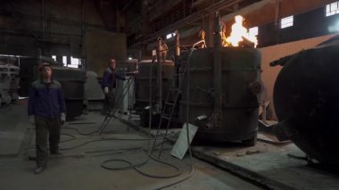Endüstriyel işçiler bir metal dökümhanesinde, erimiş metal dökme ve dökme sürecini gösteren bir fırın işletiyorlar.