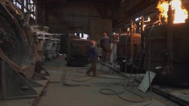 Dökümhane işçileri ağır sanayi ortamında erimiş metali kalıba döküyorlar.