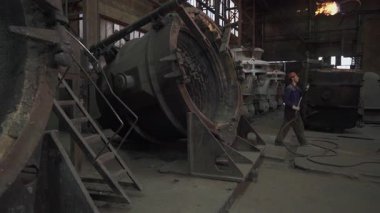 Dökümhane işçileri bir metal döküm fabrikasında ağır makineler kullanarak erimiş metali kalıplara döküyorlar.