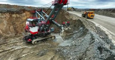 Büyük kazıcı madencilik alanında taşları çöp kamyonuna yüklüyor.