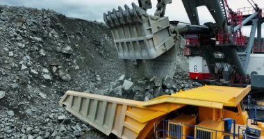 Açık bir maden ocağında büyük bir kazıcı cevheri çöp kamyonuna yüklüyor.