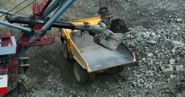 Büyük kazıcı madencilik alanında taşları çöp kamyonuna yüklüyor.