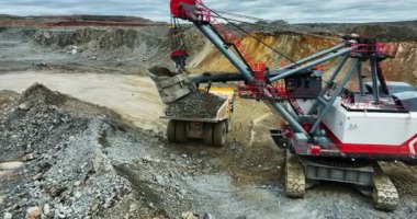 Büyük bir kazıcı açık bir madencilik operasyonunda taşları bir çöp kamyonuna yüklüyor.