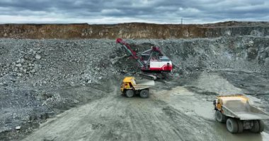 Büyük kazıcı madencilik alanında taşları çöp kamyonuna yüklüyor.