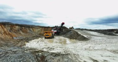 Büyük bir kazıcı açık bir maden ocağına çöp kamyonu yüklüyor.