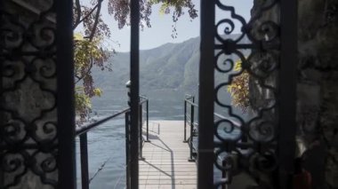 Süslü bir bahçe kapısından görünen sakin bir göl manzarası, sakin dağlar ve bereketli doğa..