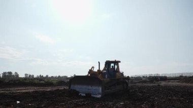 Buldozer güneşli bir günde inşaat alanında toprağı hareket ettiriyor. Kırp