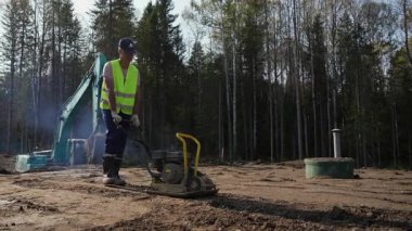 İnşaat işçisi inşaat alanındaki toprağı sıkıştırmak için titreşimli plaka sıkıştırıcısı kullanıyor. Kırp